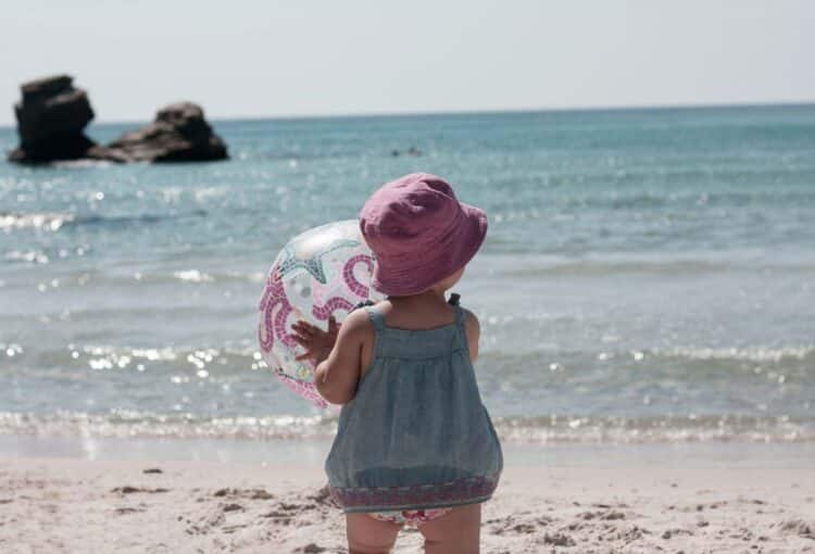 a little girl holding an inflatable ball at the beach, a moment that reminds every mom to soak up every minute with their kids