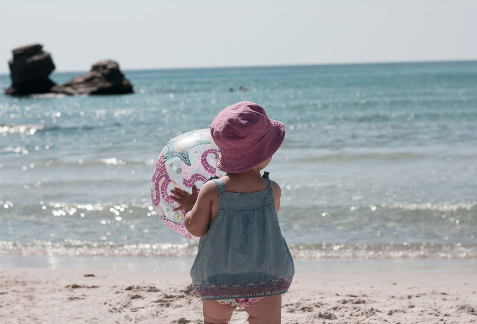 a little girl holding an inflatable ball at the beach, a moment that reminds every mom to soak up every minute with their kids