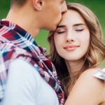 a woman smiling while being kissed on the forehead by her green-flag man