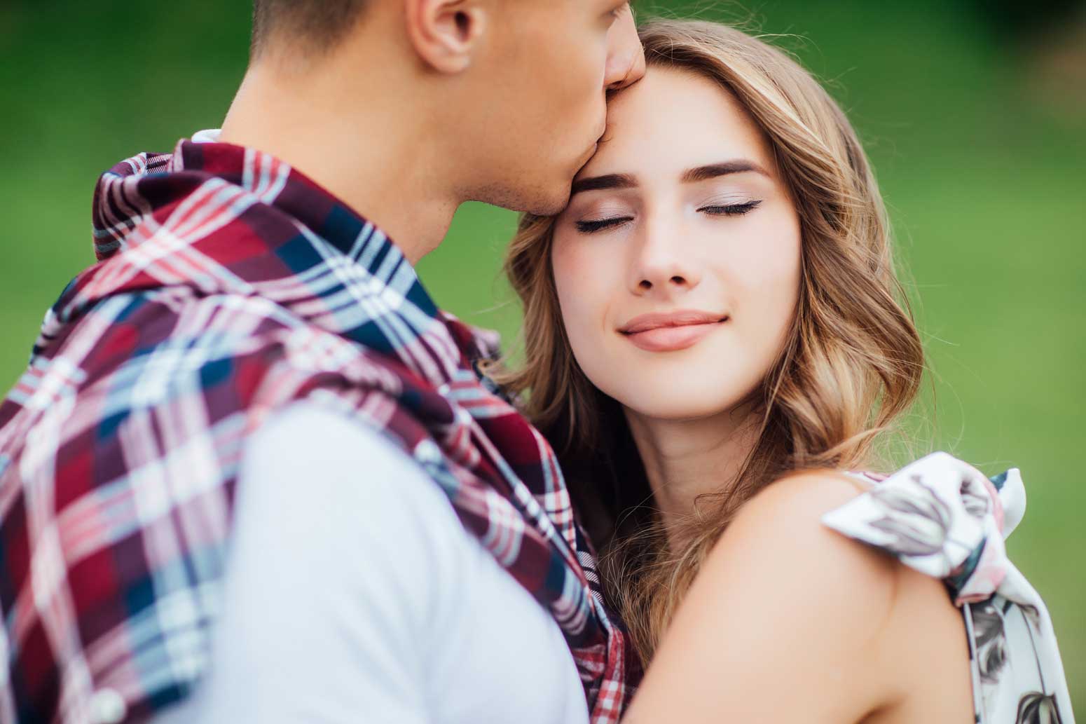 a woman smiling while being kissed on the forehead by her green-flag man