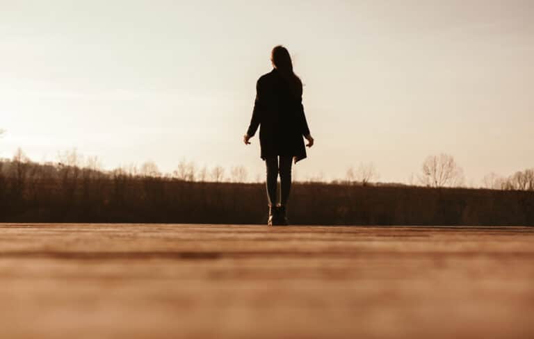 ground-level view of woman from behind walking on a road reflecting after a friend's death