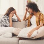 two women sitting on a couch in distress since one is leading an unhealthy life