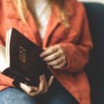 woman sitting down and thumbing through a Bible, one of a few morning practices to draw closer to Jesus