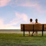 after pondering what steps to take when you start dating again, a couple sits together on a bench at sunset