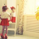 a little girl in her mom's heels studies herself in a mirror, underscoring the importance of protecting your child's self-worth