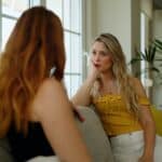 two young women sit on a couch facing each other with a grim expression on their face as they contemplate how to restore a broken relationship