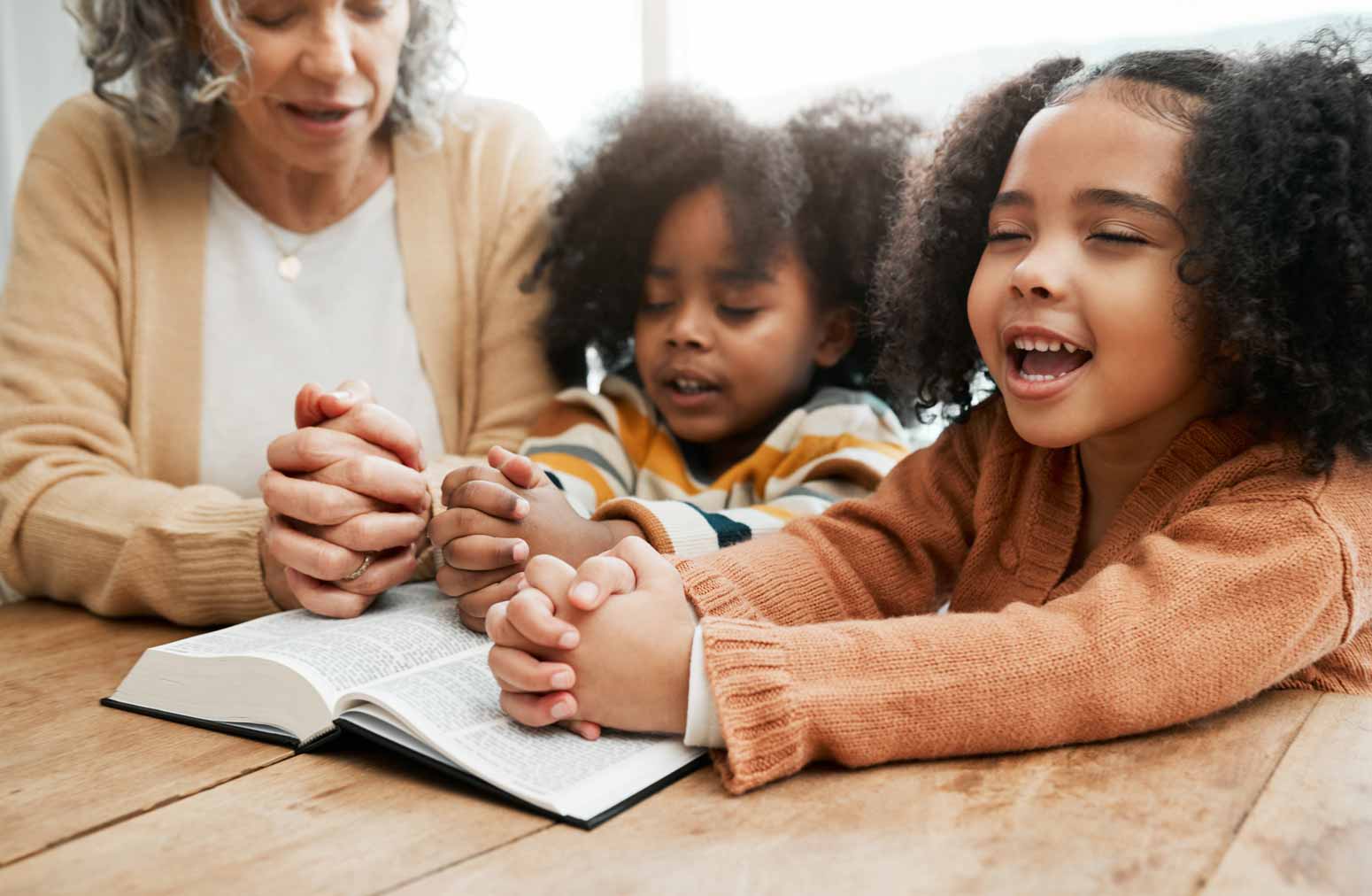 woman cultivates her young children's faith by praying over a Bible with them