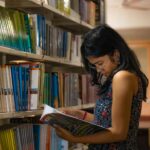 young girl reading a book between the library stacks at a community college