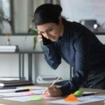 Christian woman in business on the phone leaning over a work table