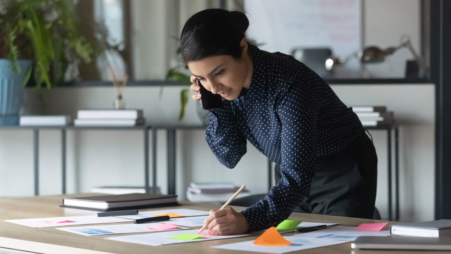 Christian woman in business on the phone leaning over a work table