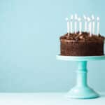 a chocolate cake with candles sitting on a blue pedestal, an example of many types of birthday freebies one can claim