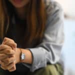 woman seated with her hands clasped on top of her knees