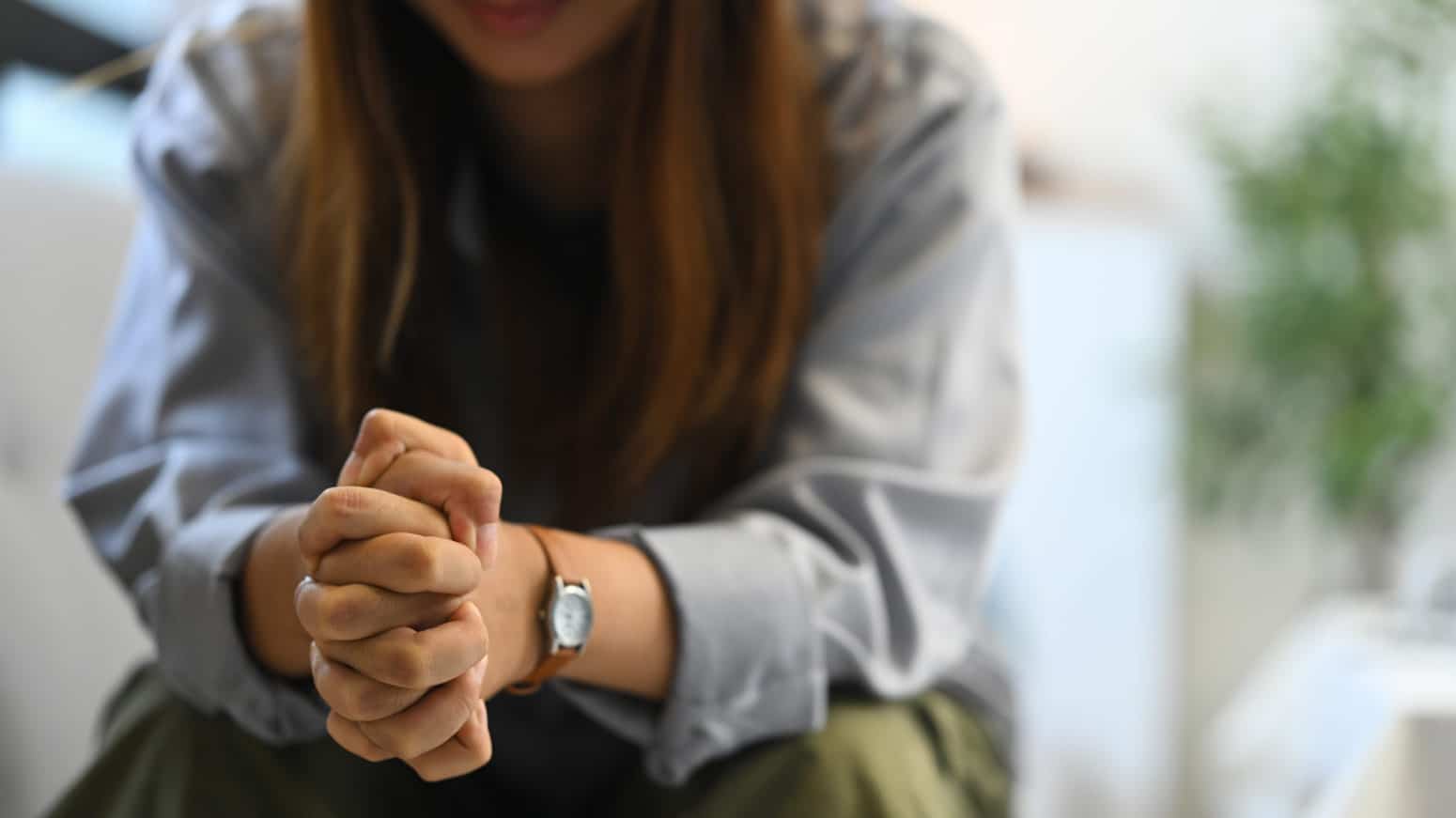 woman seated with her hands clasped on top of her knees