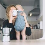 tired mom holding baby in one hand and drinking coffee in the other because it isn't selfish to take time for yourself