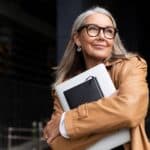 older woman holding books and papers close to her chest smiles, illustrating contentment after finding your calling