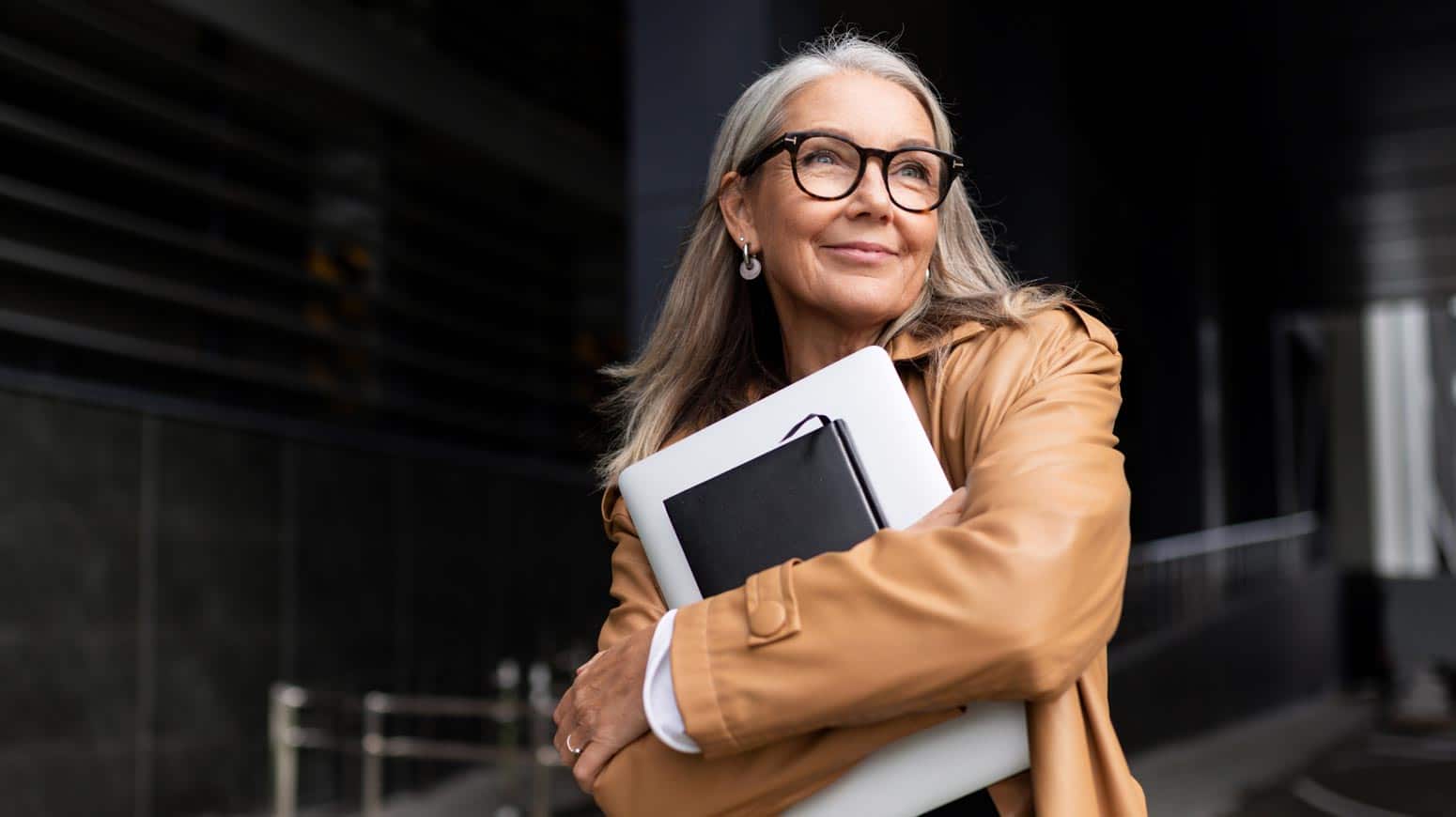 older woman holding books and papers close to her chest smiles, illustrating contentment after finding your calling