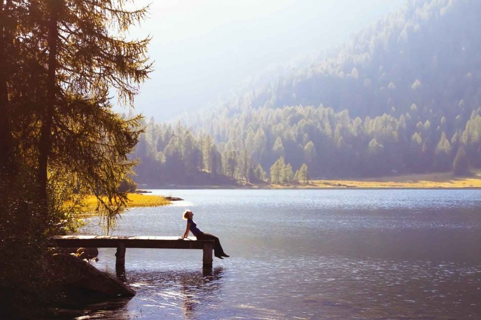 woman at the edge of a dock over a mountain lake, looking up at the sky and contemplating true hope
